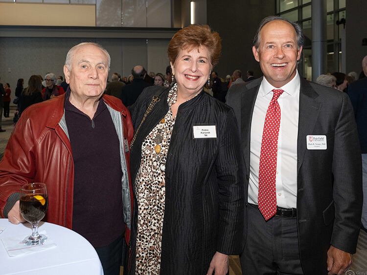 Joseph and Robbin Kanarek with President Nemec smiling and posing together at an indoor event. The background shows a crowd in a well-lit room, creating a warm and sociable atmosphere.
